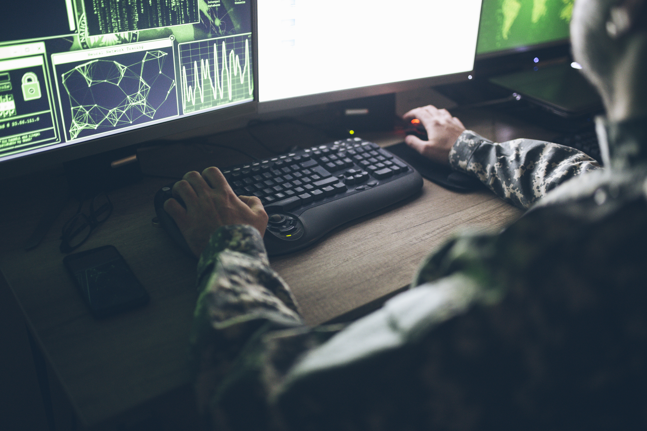 Soldier seated at a computer in a dark room.
