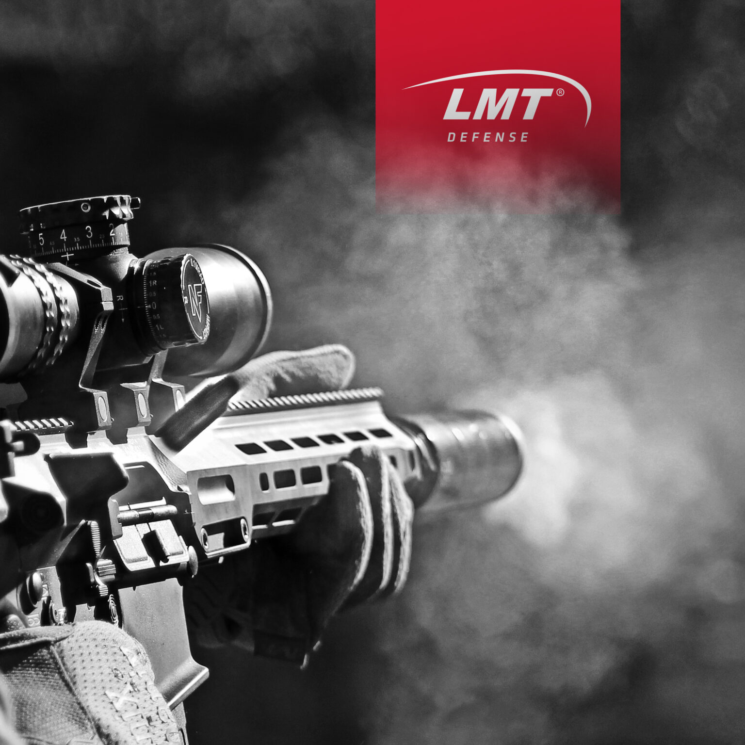 Black and white over-the-should view of man in sunglasses firing a high-powered automatic rifle with LMT Defense logo in the background.